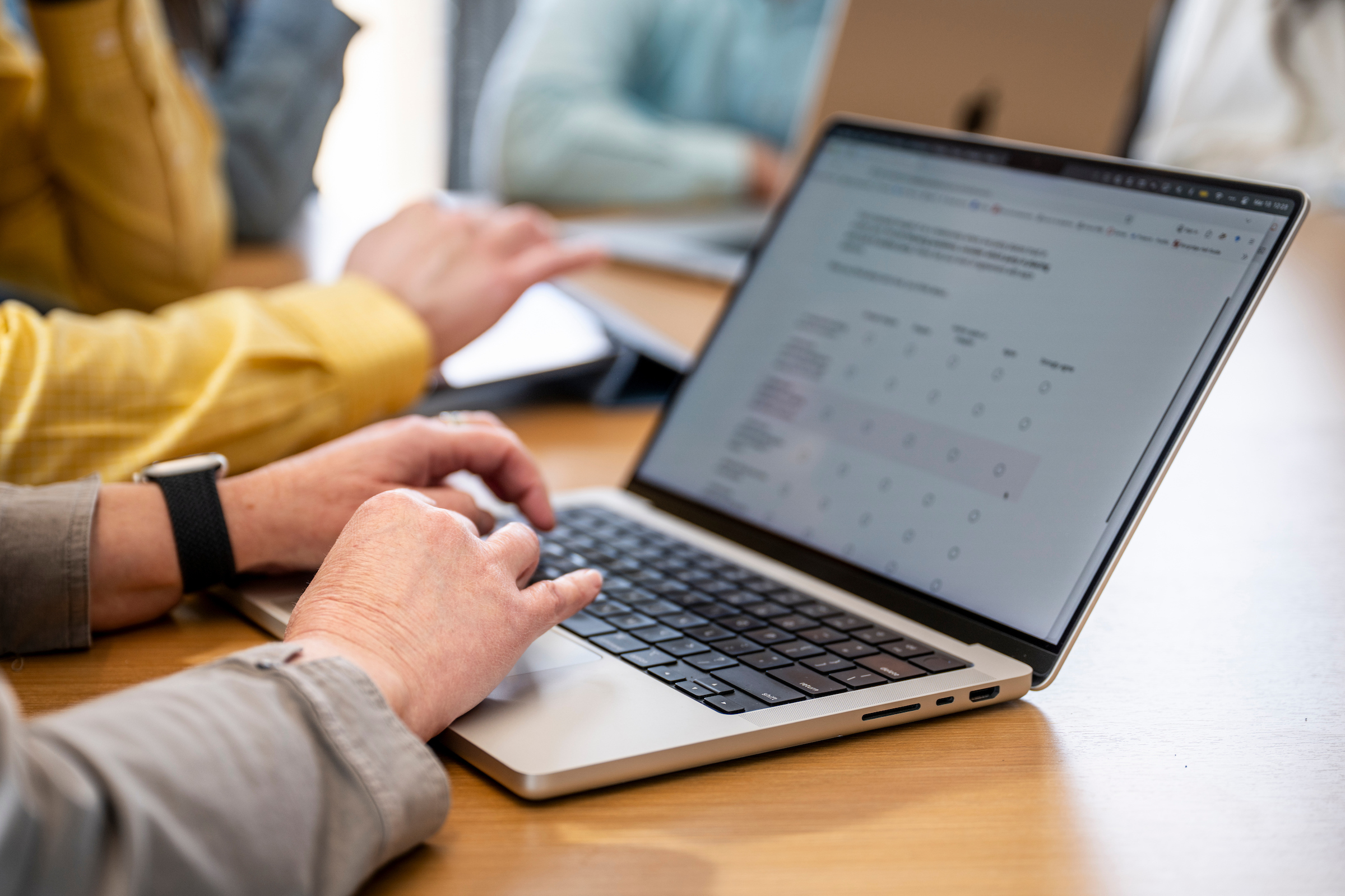 An open laptop sitting on a table with a person's hands on the keyboard.