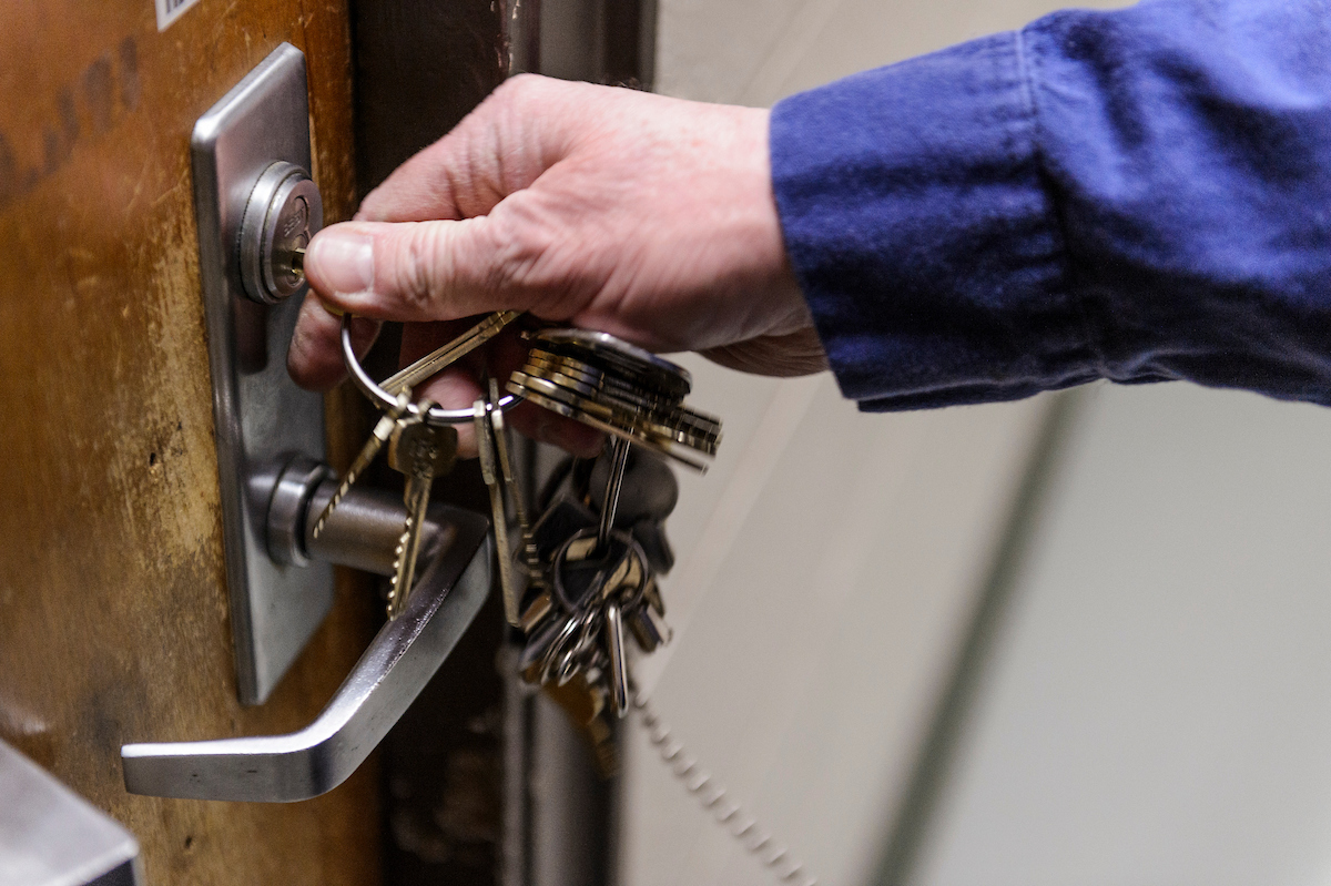 An arm in a blue dress shirt unlocking a door using a keyring that has many keys on it.